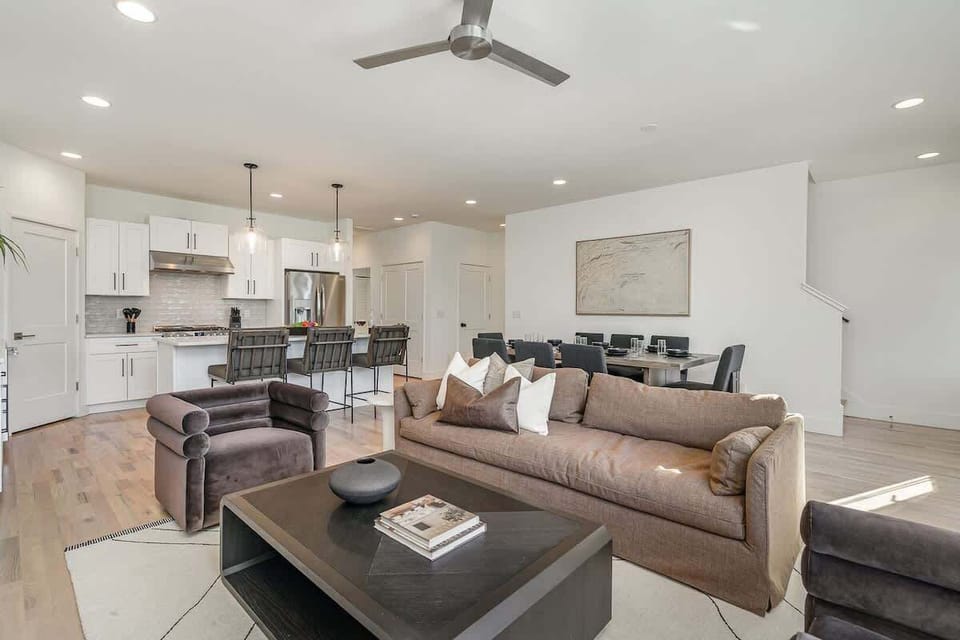 Relax in the cozy living room with ample seating, a flat-screen TV, and natural light pouring through large windows.