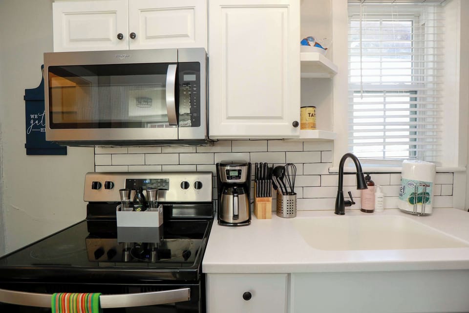 Kitchen with stove, oven, coffee maker, utensils, storage space, micrwave, a window and soap. 