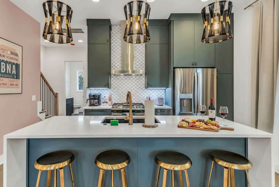 The kitchen island anchors this modern space: dark green cabinetry, four stools, a stove, and range hood make group cooking feel effortless and fun