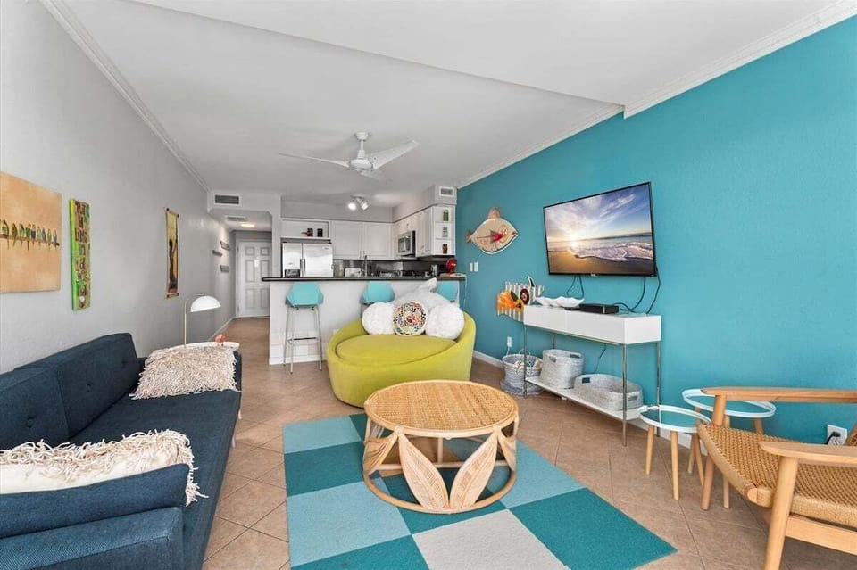 Spacious living room with comfortable seating, wall-mounted TV, coastal décor, and seamless flow into the kitchen and dining area.