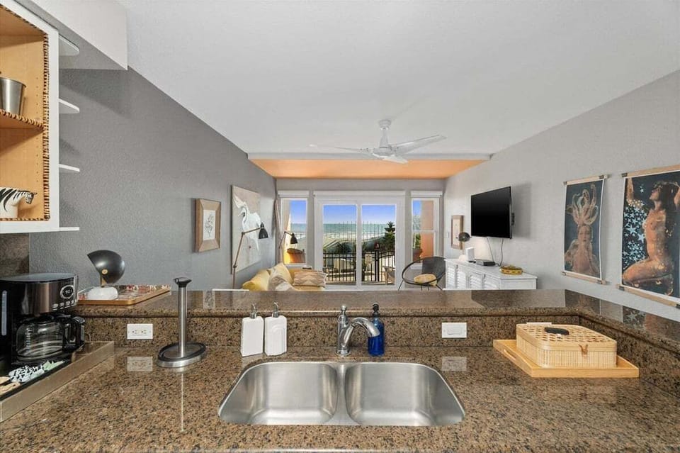 Kitchen breakfast bar with granite counters, double sink, open living area, and Gulf-view balcony beyond.