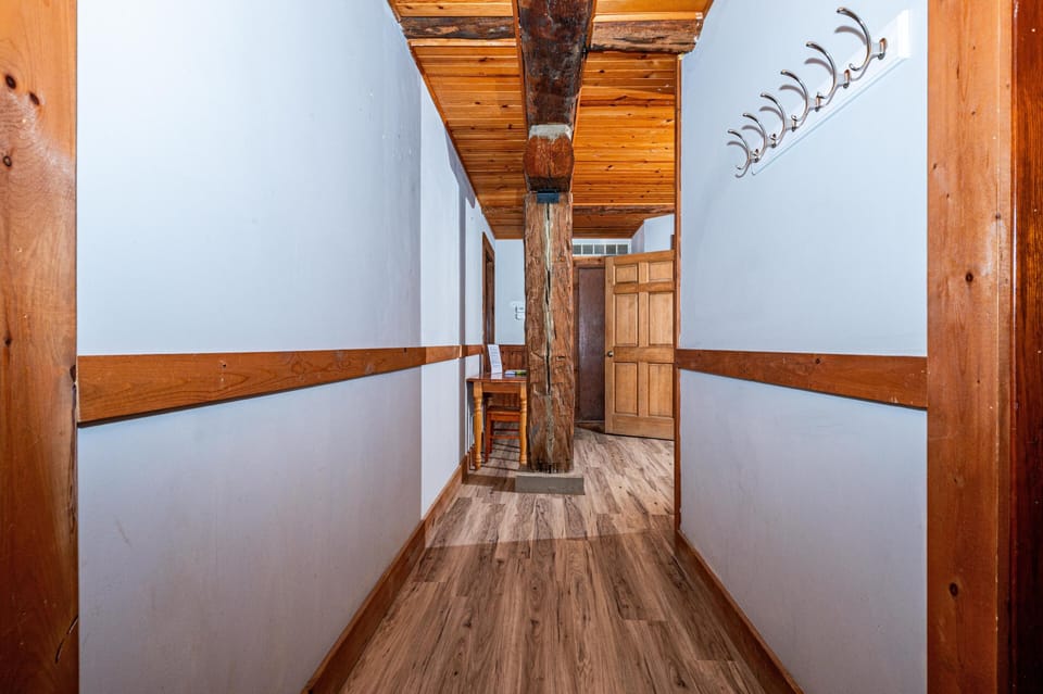 Hallway with light blue walls, wood trim, wood-look flooring, ceiling paneling, and a central rustic support beam.