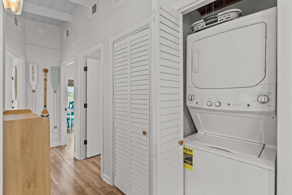Convenient Oak Island NC laundry area with stacked washer and dryer, hallway access, and coastal decor, making it easy to refresh beach towels and clothes during your stay.