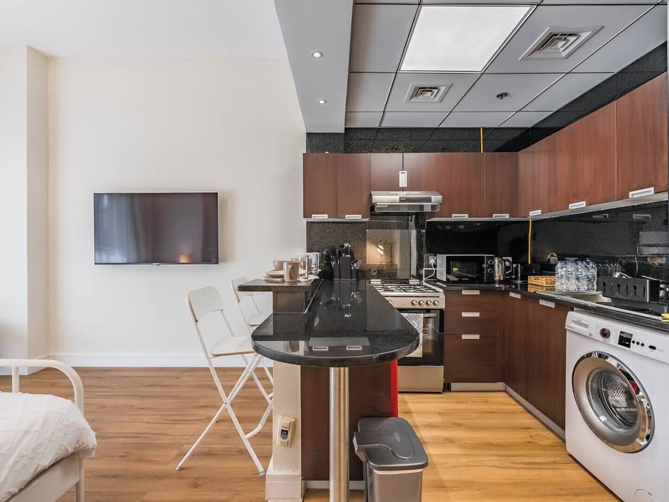 A stylish, contemporary kitchen boasting elegant granite countertops, warm wooden cabinets, top-of-the-line appliances—including a washing machine—and a chic bar-style dining area—perfectly blending beauty and functionality.