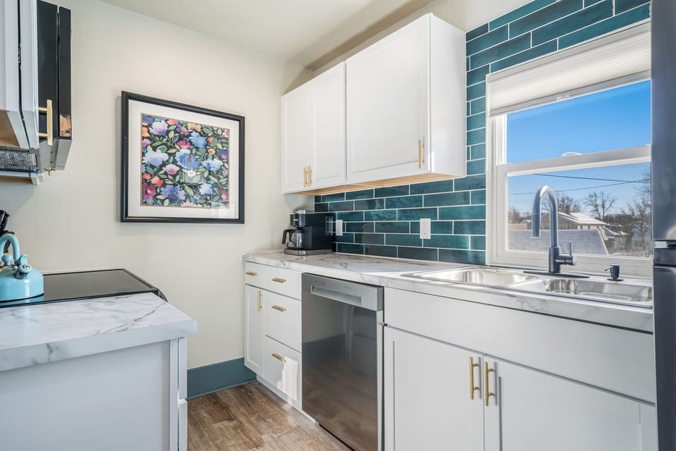 - Modern kitchen with marble-style countertops and teal backsplash design   - Equipped with stainless steel appliances and sleek white cabinetry   - Bright window lighting enhances this fresh and functional cooking space