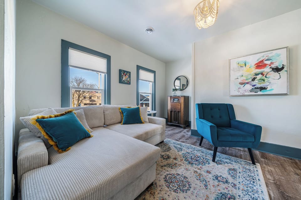 - Bright living area with cozy sectional and teal accent chair for relaxing afternoons   - Modern décor, colorful art, and streaming-ready TV create a stylish lounge vibe   - Natural light and warm tones make this living space your perfect comfort corner