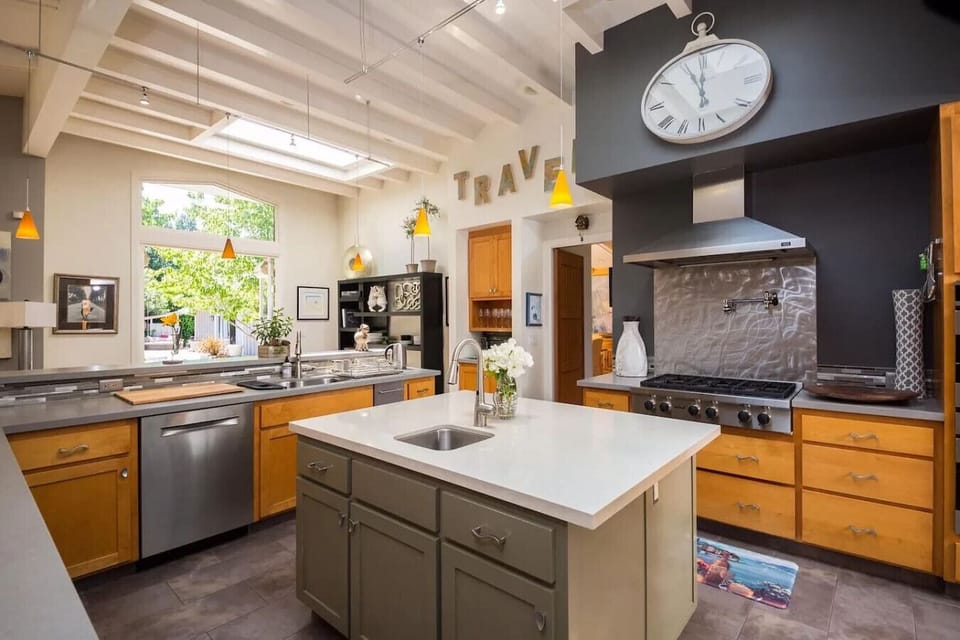 Spacious modern kitchen featuring stainless steel appliances, quartz countertops, a large center island, and charming farmhouse-style details. Perfect for home chefs, family gatherings, and entertaining guests in style. Natural light pours in through over