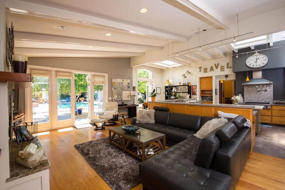 Bright and spacious open-concept living area featuring vaulted ceilings, exposed beams, and elegant French doors leading to a private backyard oasis. This modern layout seamlessly connects the gourmet kitchen, dining, and living room — perfect for enterta