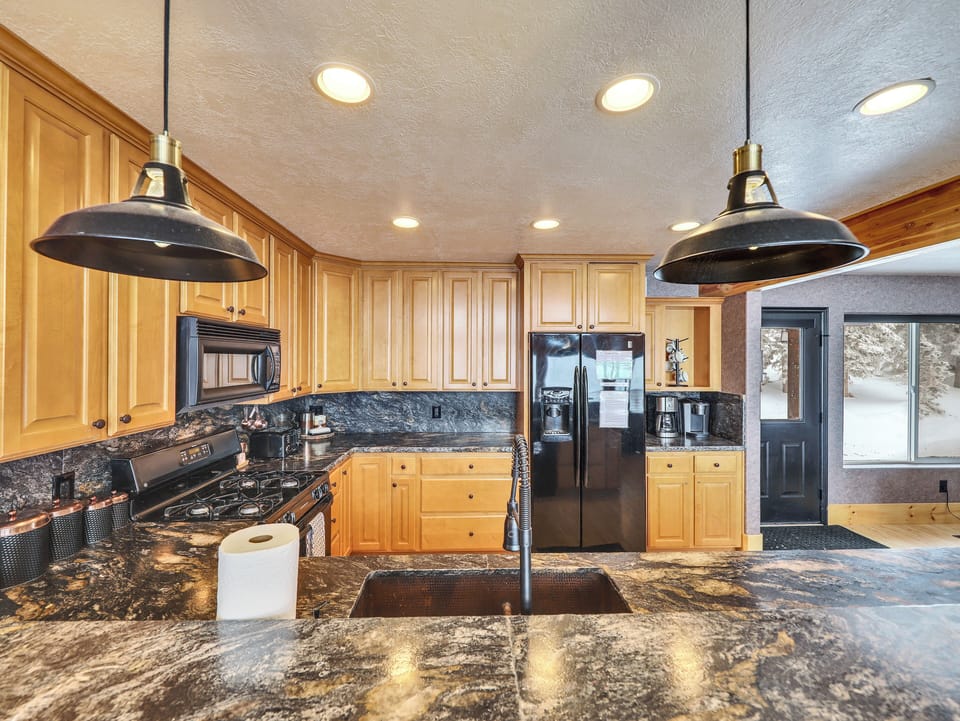 Gourmet kitchen fully equipped with top-of-the-line appliances, stone countertops and backsplash, custom lighting, and a spacious counter with seating for four