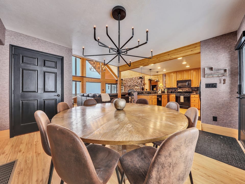 Dining area featuring custom lighting, full-length windows with forest views, and a round dining table that seats nine.