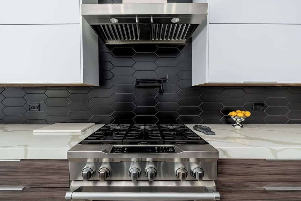 Prepare your favorite meals on a professional-grade gas range with sleek modern finishes and stylish hexagon tile backsplash in this fully-equipped kitchen.