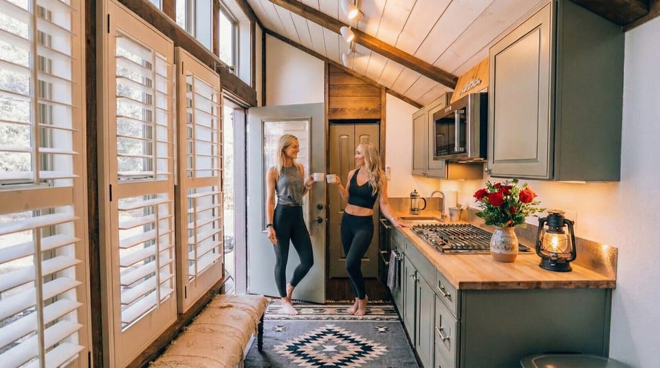 The open-concept interior features soaring ceilings, oversized windows, a fully equipped kitchenette, and stylish furnishings designed to maximize comfort in a beautifully crafted tiny home.