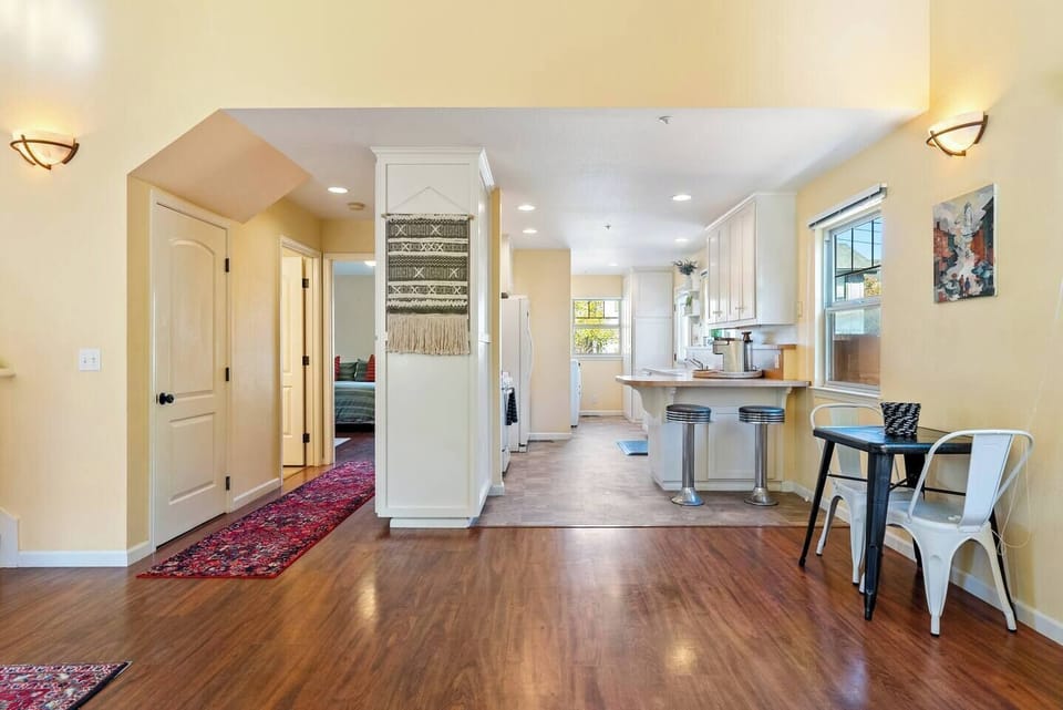 A vibrant open-concept layout, showing a decorative wall hanging, warm wood flooring, and a clear view from the dining nook into the kitchen.