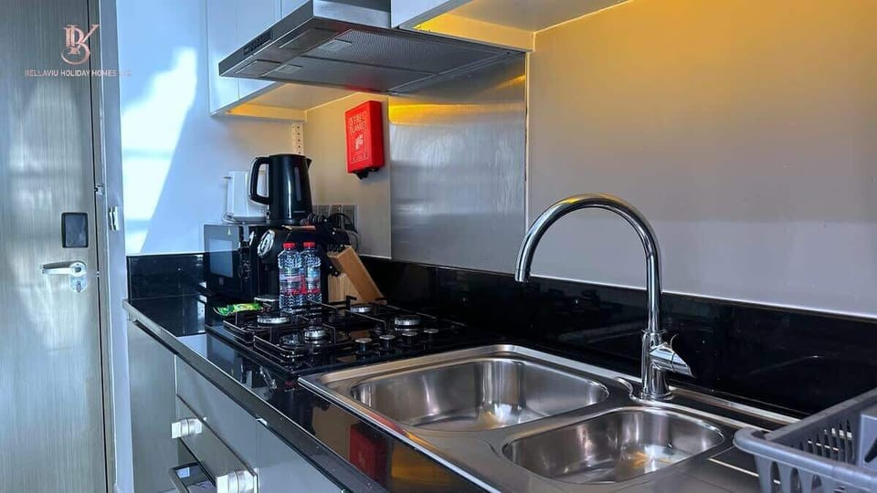 A modern kitchen features sleek cabinets, smooth countertop, and stainless steel appliances. Natural light floods the space, highlighting minimal décor, a tidy sink, and neatly arranged utensils, creating a clean, functional, and inviting atmosphere