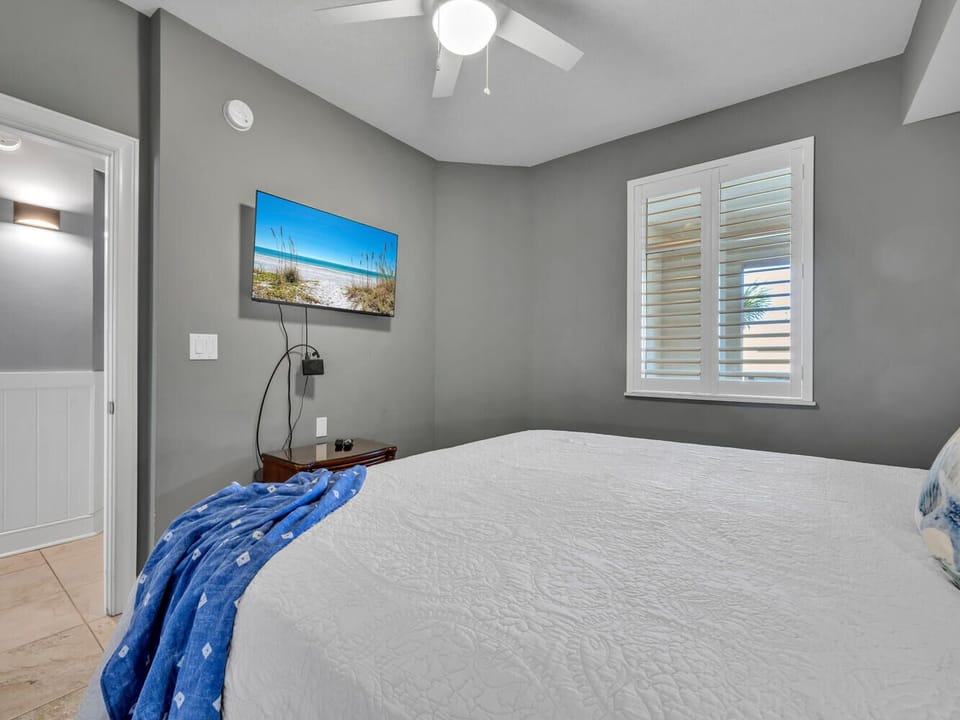 Unwind in your serene bedroom with plush bedding, coastal artwork, and modern ceiling fan for perfect comfort.
