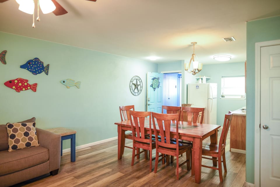 Your beachy dining space welcomes family meals with cheerful fish wall art, warm wood floors, and an open layout flowing into the kitchen.