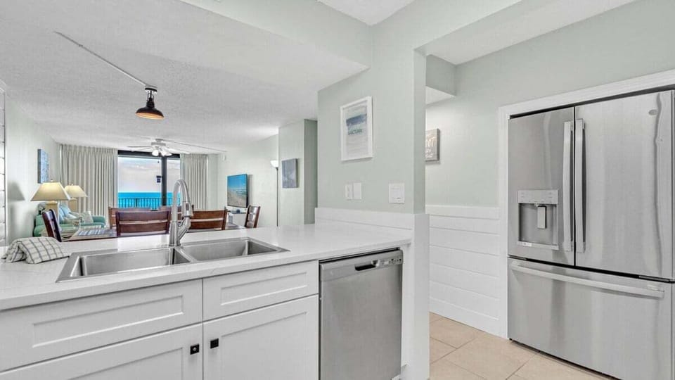 This bright kitchen features white shaker cabinets, stainless steel appliances, and a deep sink in a sleek, open layout.