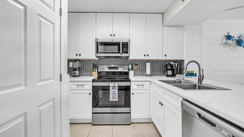 This stylish kitchen features white cabinetry, stainless steel appliances, and a striking black herringbone backsplash with ample counter space.