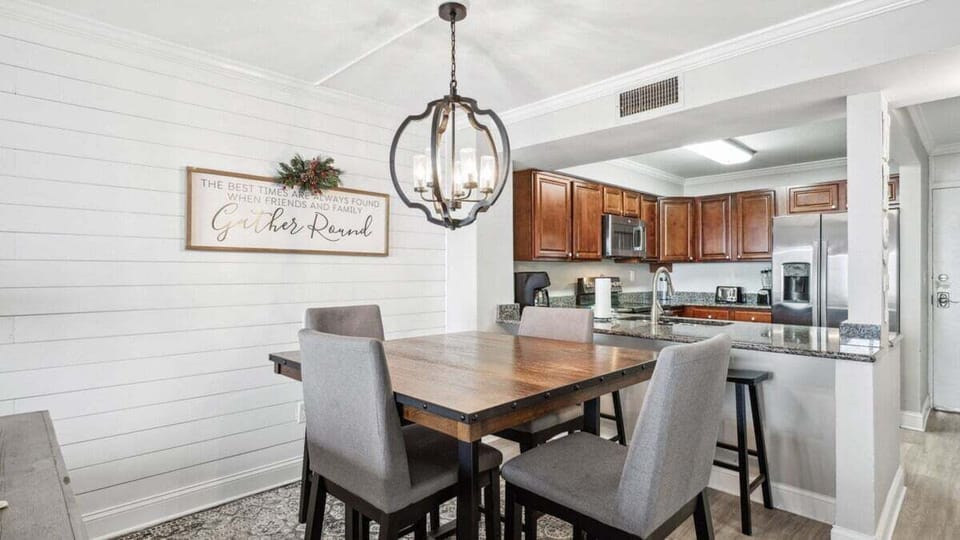 This stylish dining area has a rustic wood table for four and a modern chandelier, perfect for meals near the kitchen.