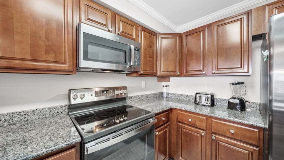 This modern kitchen features granite countertops, stainless steel appliances, ample cabinet space, and essential appliances like a blender, toaster, and microwave.