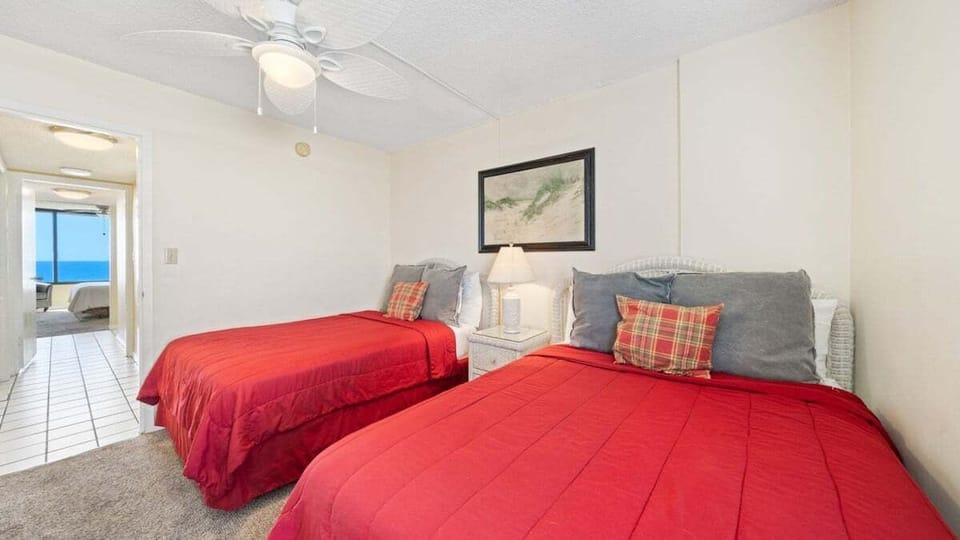 Cozy and Bright. This guest bedroom features two comfy full beds, soft lighting, and a peek of the ocean down the hall — perfect for relaxing after a day at the beach.