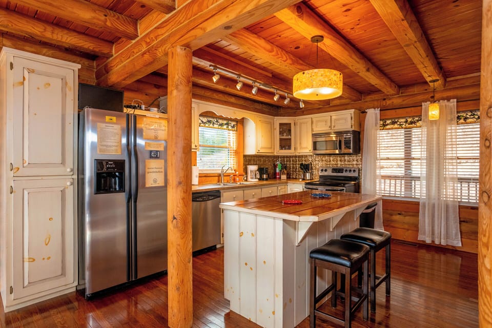 Bright and spacious kitchen with a rustic-modern vibe, featuring a central island with bar seating, warm wooden beams, and stainless steel appliances—perfect for cooking and socializing.