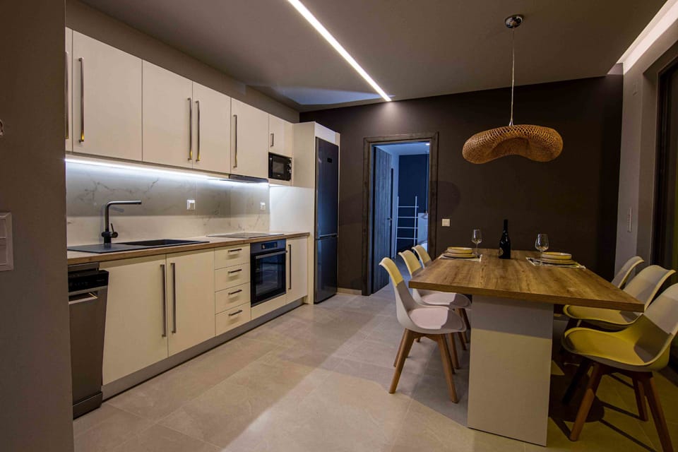 An open-plan kitchen with rustic wooden cabinets, modern appliances, and a sunlit dining table ready for long, relaxed meals