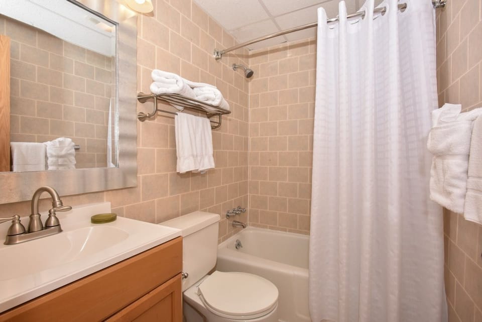 Bright and modern bathroom with tiled walls, a spacious vanity, and a full shower-tub combination for comfort and convenience.