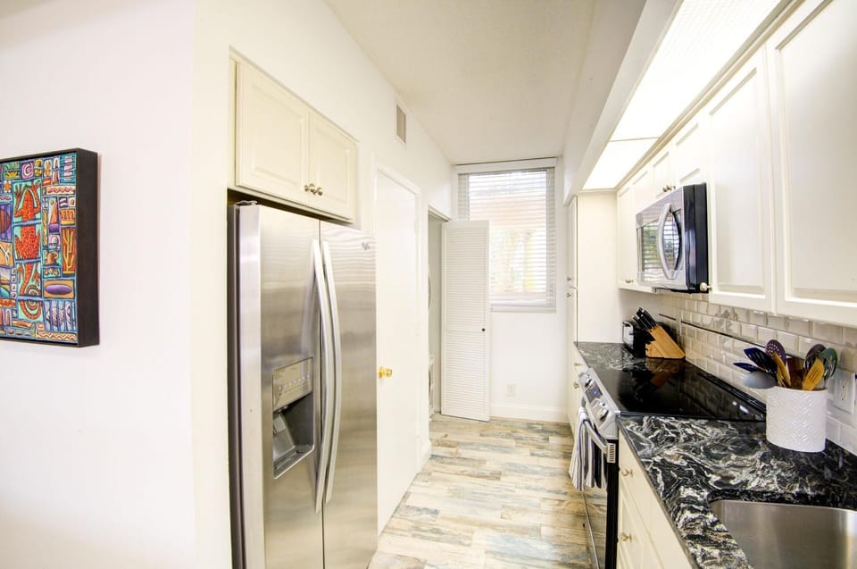 Galley kitchen with black-and-white marbled countertops, subway tile backsplash, and stainless steel appliances.