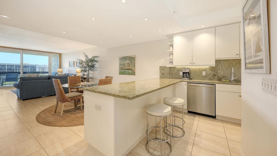 Kitchen with granite countertops, white cabinets, stainless steel dishwasher, and two white cushioned bar stools.