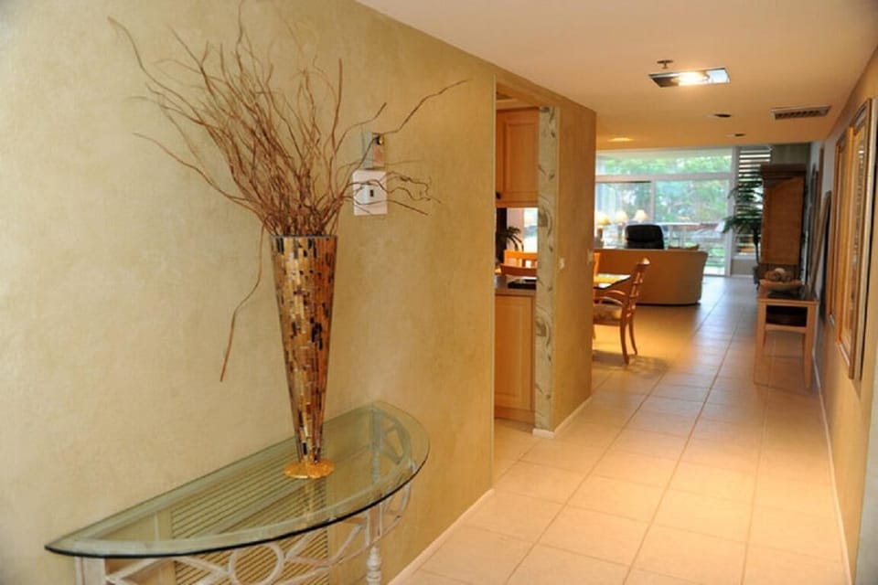 Glass-top console table with mosaic vase and twigs sits along hallway leading to dining and living areas.