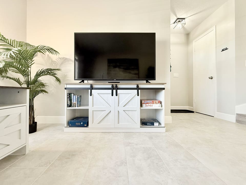 Well-lit living room, featuring a large window, L-shaped sofa, and TV 