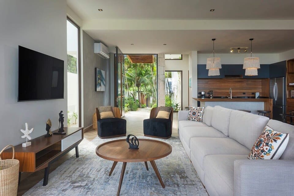 Modern living room with a spacious and comfortable sofa. It features two individual armchairs, a TV, and AC.