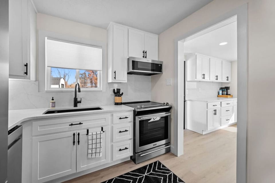 Contemporary chalet kitchen featuring tailor-made quartz countertops and brand-new appliances, effortlessly flowing into a sunlit laundry area and coffee bar. This space opens up to the backyard patio, providing plentiful cabinetry and an airy layout