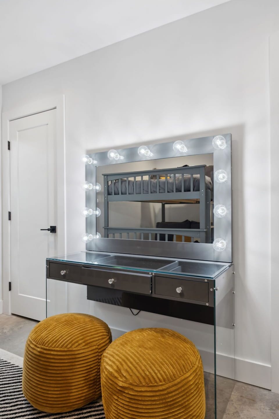 Elegant glam station with a mirror framed by lighting and modern, plush seating.