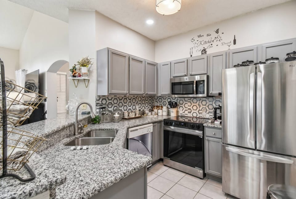 Experience a stylish kitchen featuring sleek gray cabinetry and a vibrant patterned backsplash. Enjoy spacious granite countertops for effortless meal prep and modern appliances that enhance your culinary adventures.