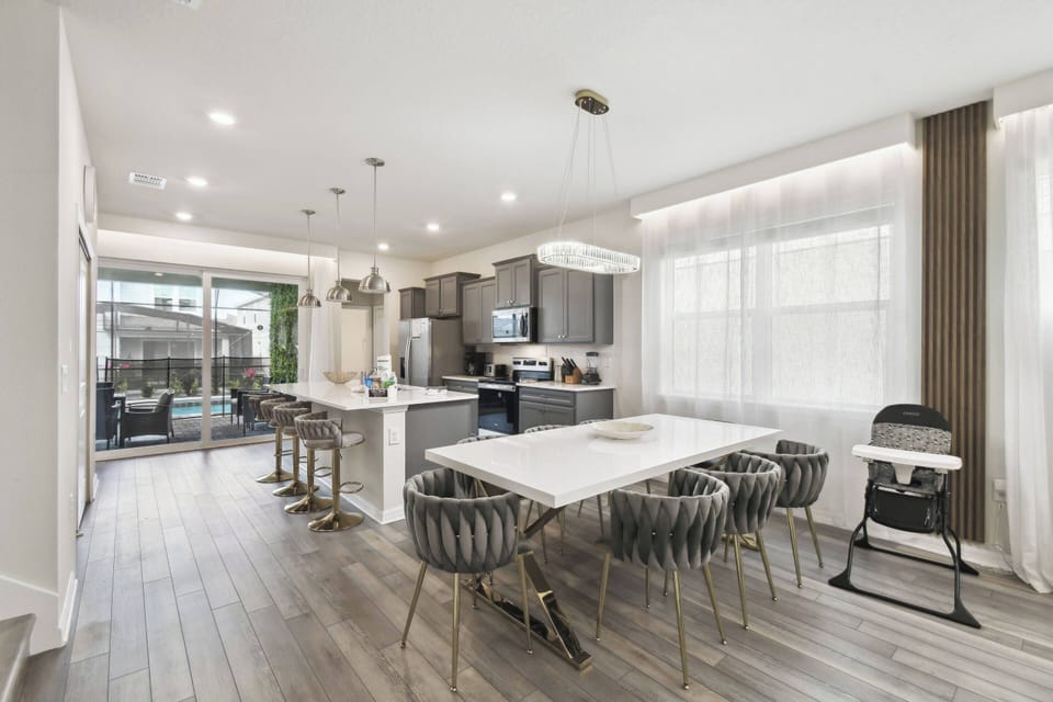 Enjoy a bright and airy dining area with a sleek white table and stylish gray chairs, ideal for gathering with loved ones. Large windows fill the space with natural light, seamlessly connecting to a cozy outdoor area.