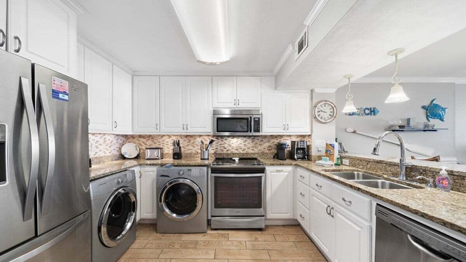 This updated kitchen features stainless steel appliances, granite counters, in-unit laundry, and coastal-style finishes.