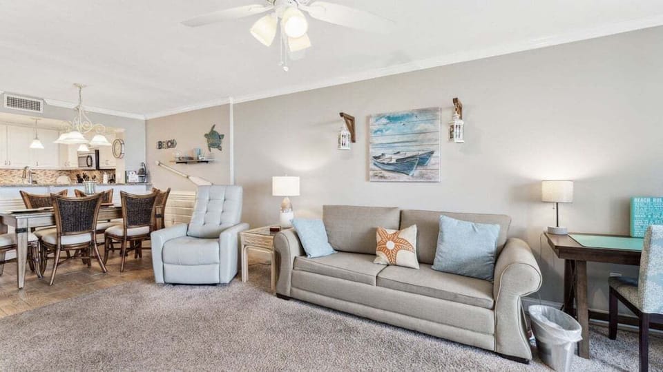 This cozy living space includes a neutral sofa, recliner, coastal décor, dining area, and writing desk in an open layout.