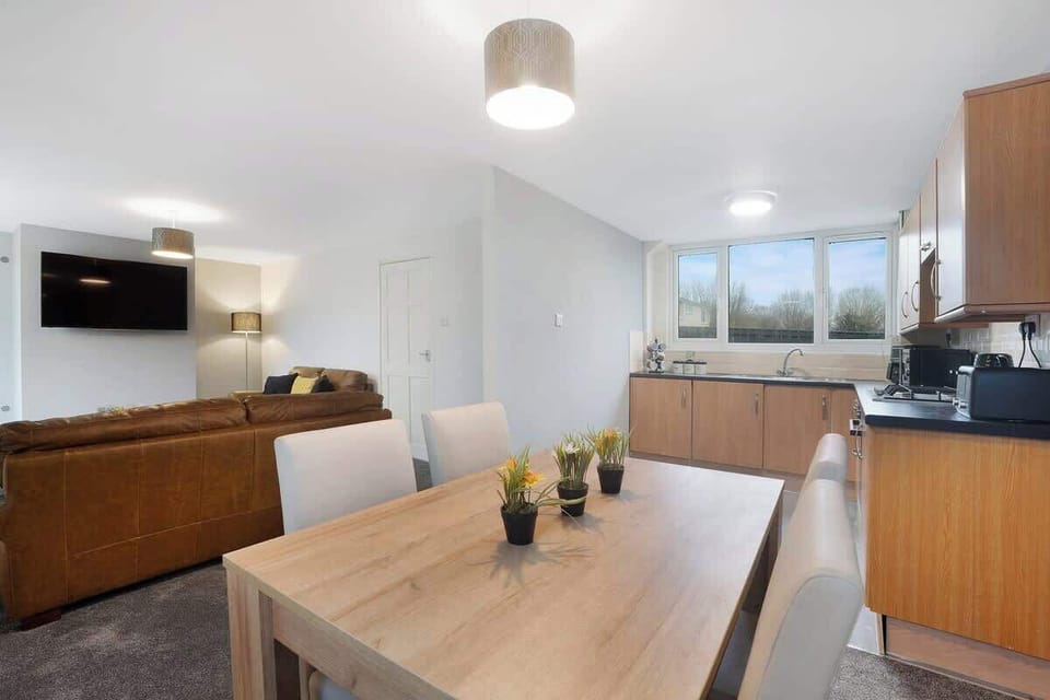 The dining area, adjacent to the kitchen, features a rustic wooden table with seating for four. A stylish pendant light hangs overhead, providing a warm ambiance. Large windows let in natural light, while soft drapes add a touch of elegance. 