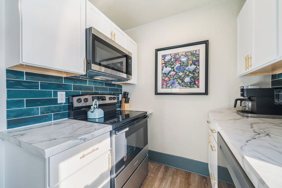 Enjoy this compact yet efficient kitchen with ample storage in white cabinets accented by gold handles. A built-in microwave and oven make cooking convenient, while a blue tile backsplash adds a splash of color. 