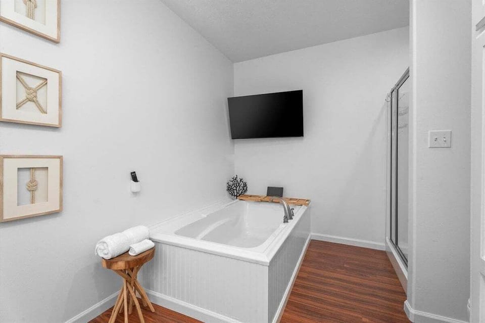 Primary bathroom soaking tub with wall-mounted Smart TV, hardwood-style flooring and a nearby glass-enclosed shower for a relaxing spa-inspired experience.