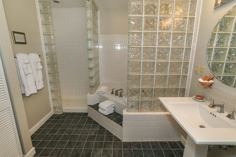 Spacious bathroom featuring a luxurious soaking tub, sleek glass accents, and a modern pedestal sink.