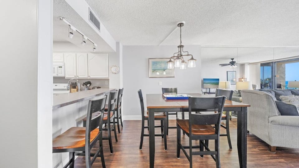 Enjoy casual meals and conversations in this open dining area with a breakfast bar and coastal lighting, flowing into the kitchen and living room.