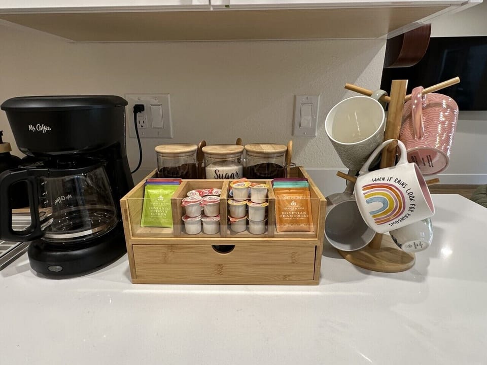 Well-organized coffee station with a drip coffee maker, pods, teas, and sweeteners, plus a selection of mugs. Perfect for enjoying your morning brew or a relaxing cup anytime during your stay.