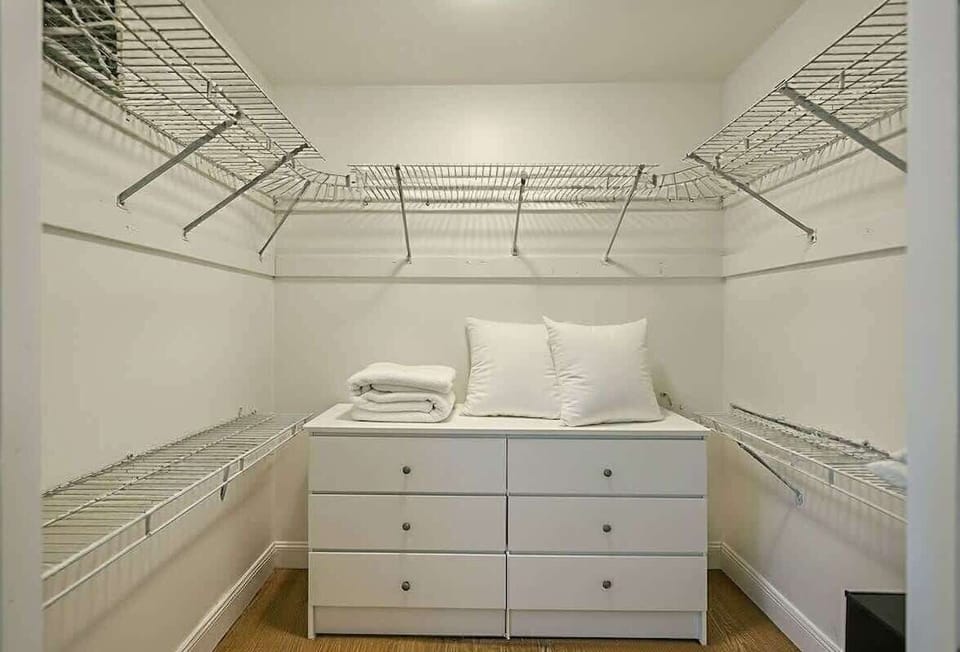 Organized walk-in closet space with shelving system, clothes hanging rod, and a spacious white chest of drawers.