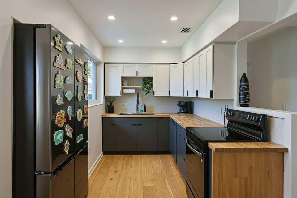 Fully equipped modern kitchen with two-tone cabinetry, black countertops, and high-end stainless steel refrigerator.