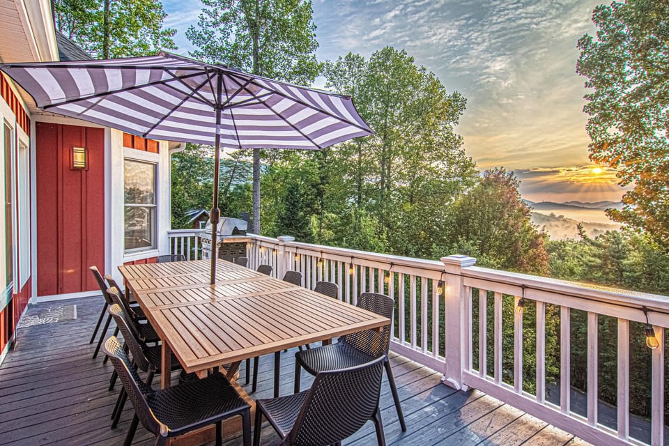 A stunning deck with a wooden dining table, black chairs, and a striped umbrella offers a perfect outdoor retreat.