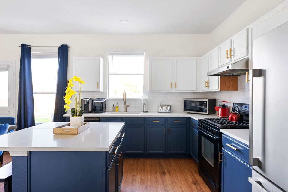 Stylish kitchen with navy and white cabinets, quartz countertops, and stainless steel appliances. Fully stocked with a gas stove, microwave, coffee maker, and more—perfect for cooking after a day at Kalahari Waterpark or from Round Rock Donuts!