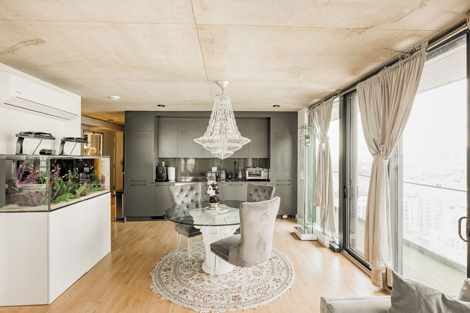 Dining area beneath a crystal chandelier with sleek concrete ceiling.

